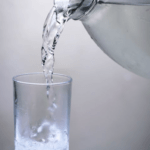 Glass being filled with water from a bottle, discussing the benefits of hot or cold water during meals.