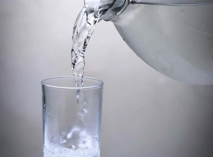 Glass being filled with water from a bottle, discussing the benefits of hot or cold water during meals.