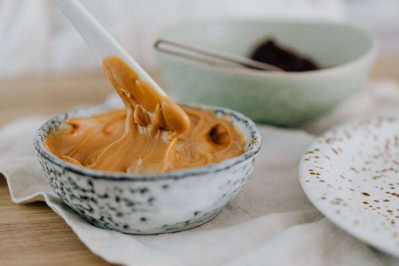 A bowl of creamy peanut butter with a spoon, placed on a table with a side dish.