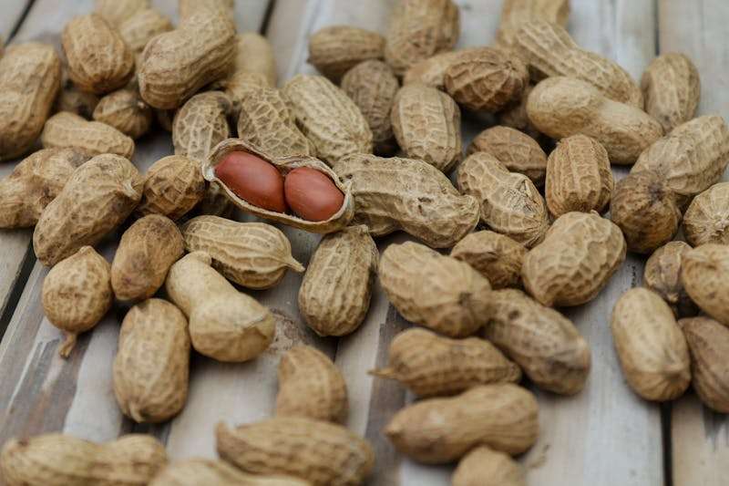 A pile of peanuts in their shells with one cracked open revealing red seeds.