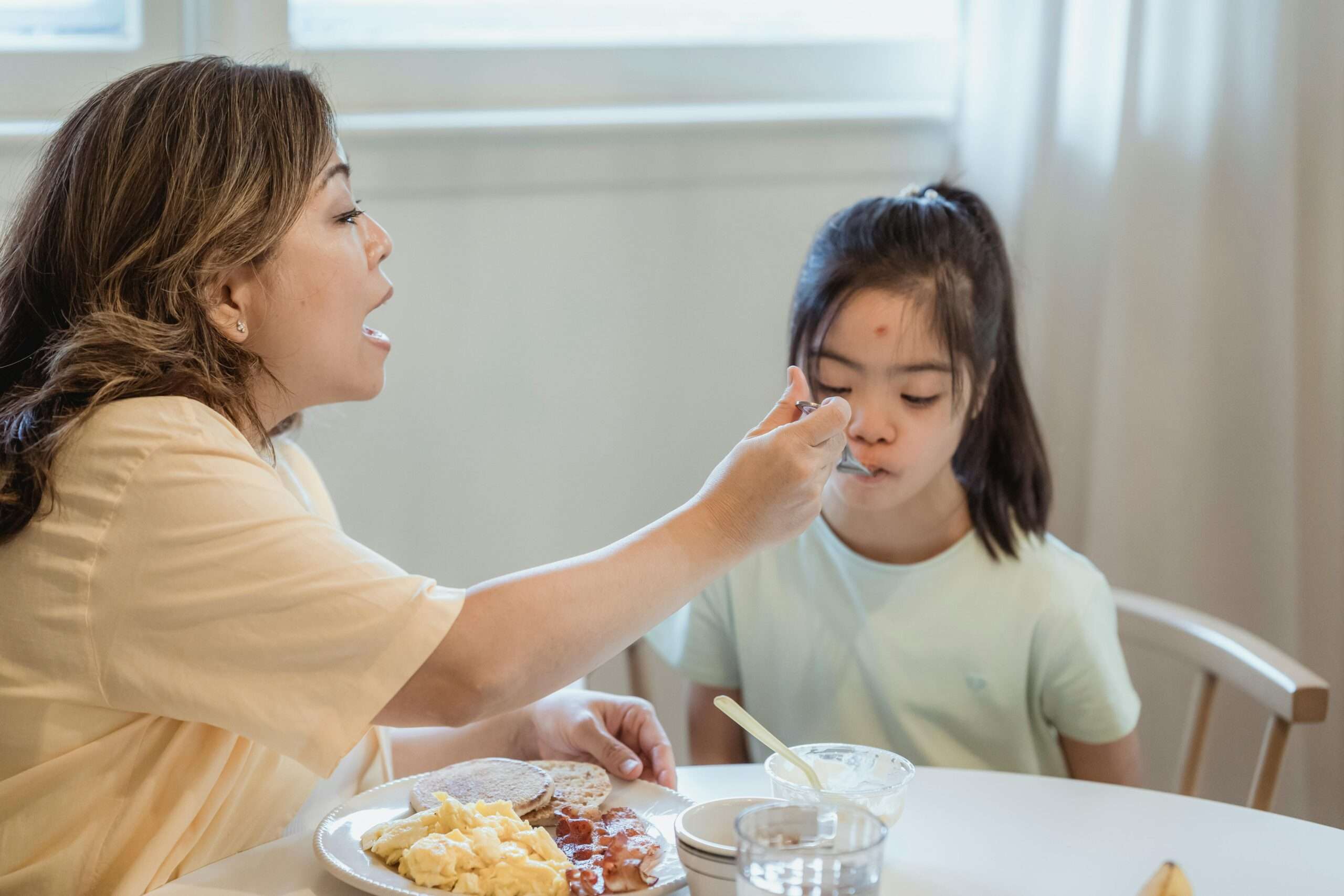 A mother feeding her autistic daughter a nutritious meal, emphasizing the Autism Diet Impact on health, digestion, and focus.